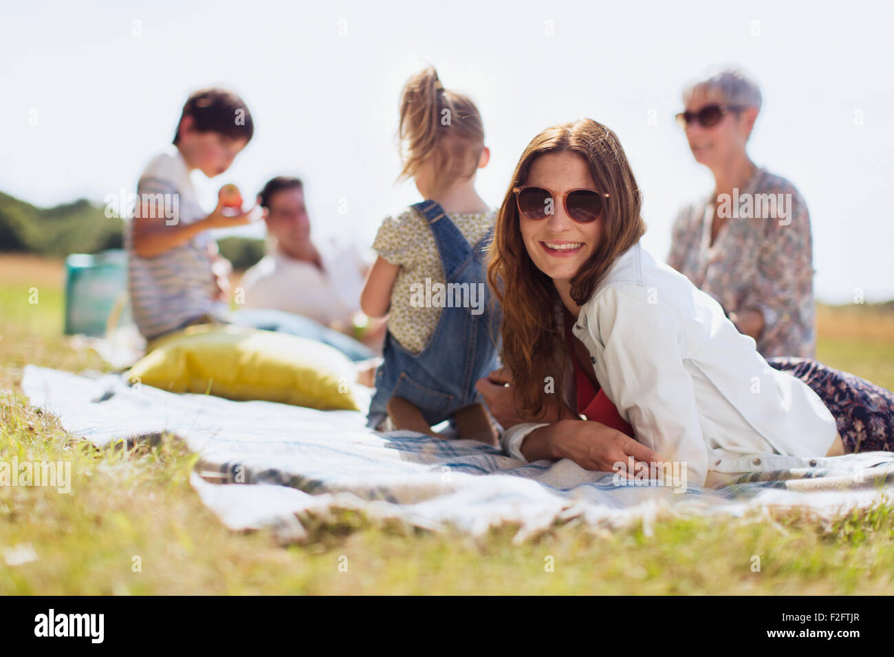 Portrait smiling woman laying on blanket in sunny field with family Stock Photo