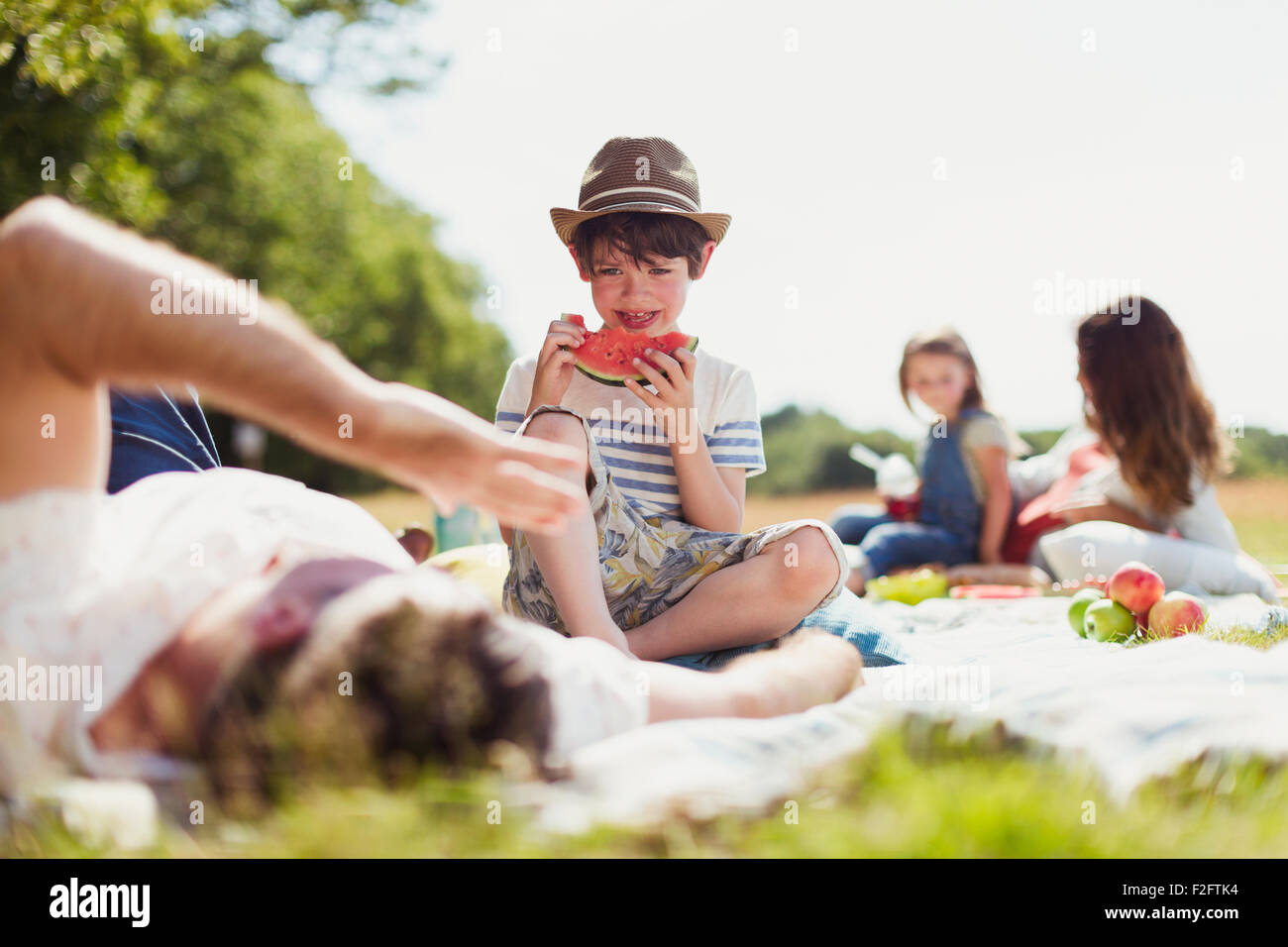 Smiling boy eating watermelon on blanket in sunny field Stock Photo