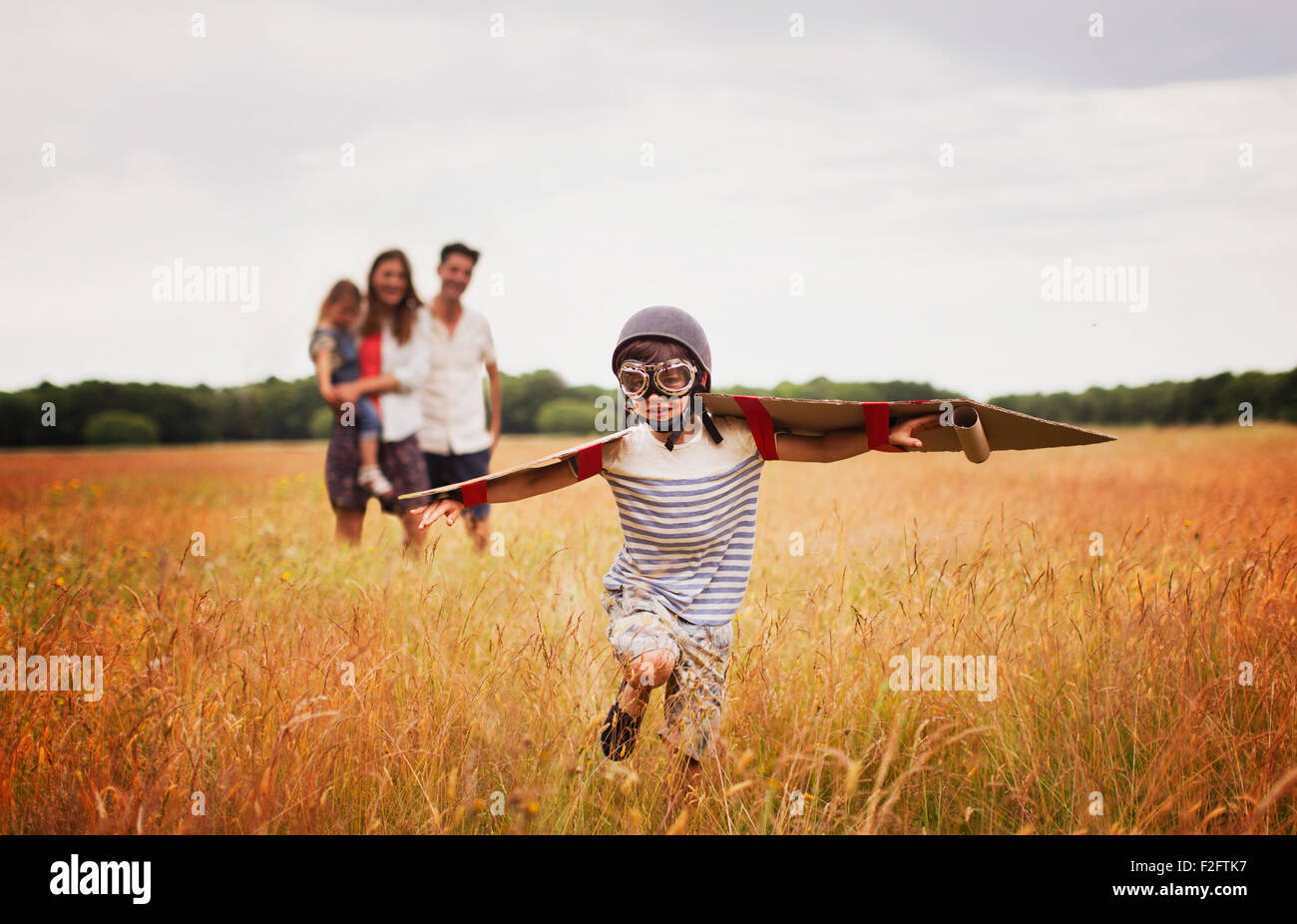 Playful boy with wings in aviator’s cap and flying goggles in field Stock Photo