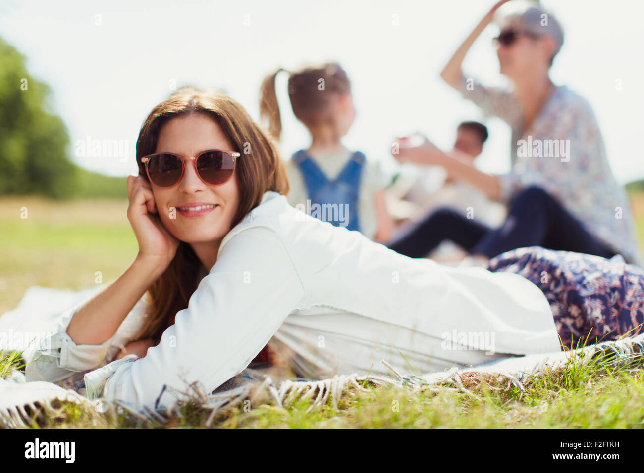 Portrait smiling woman laying on blanket in sunny field Stock Photo