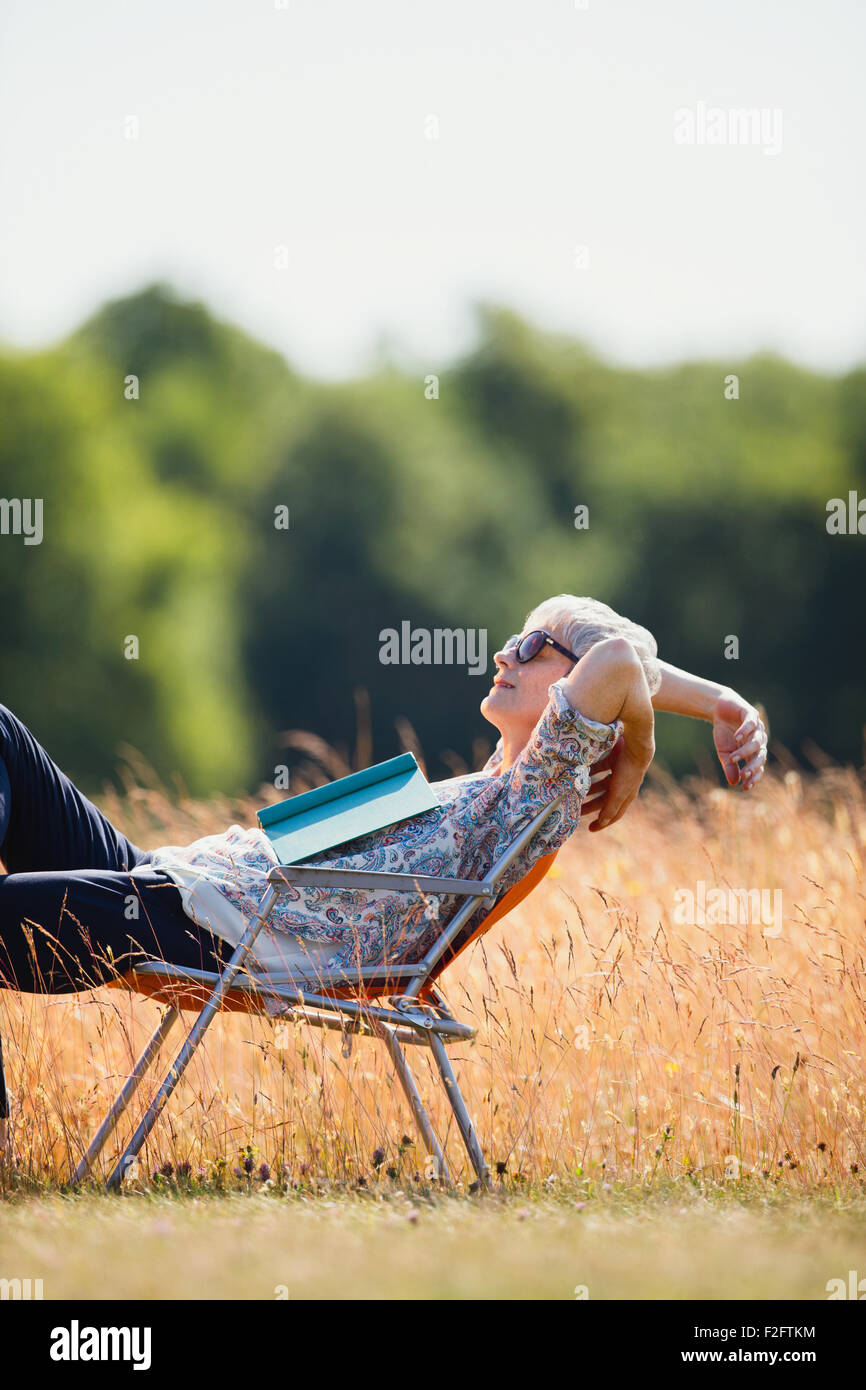 Carefree senior woman relaxing with book in sunny field Stock Photo