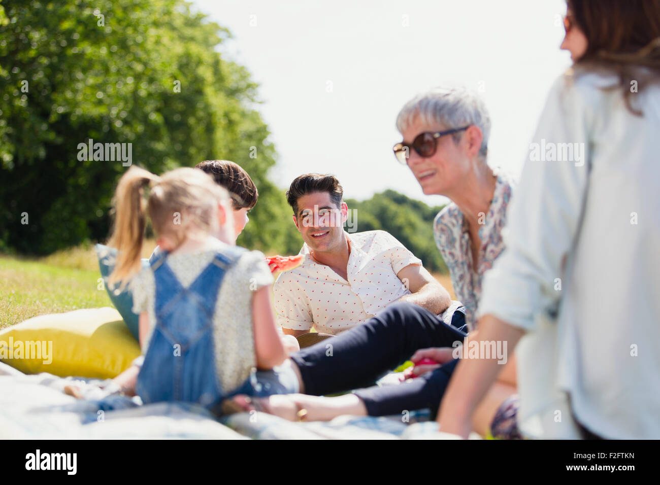 Multi-generation family relaxing on blanket in sunny field Stock Photo