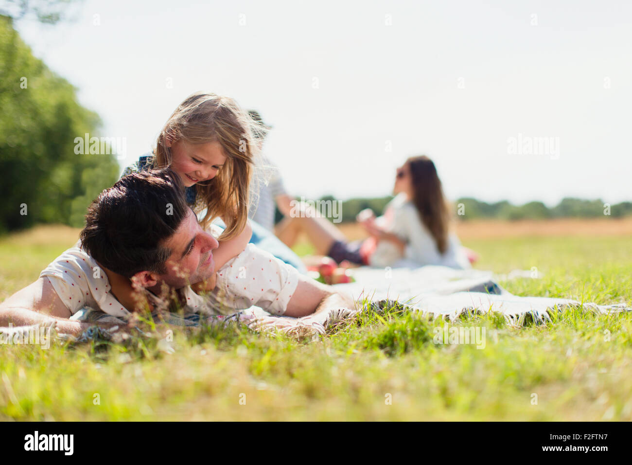 Affectionate daughter laying on top of father in sunny field Stock Photo