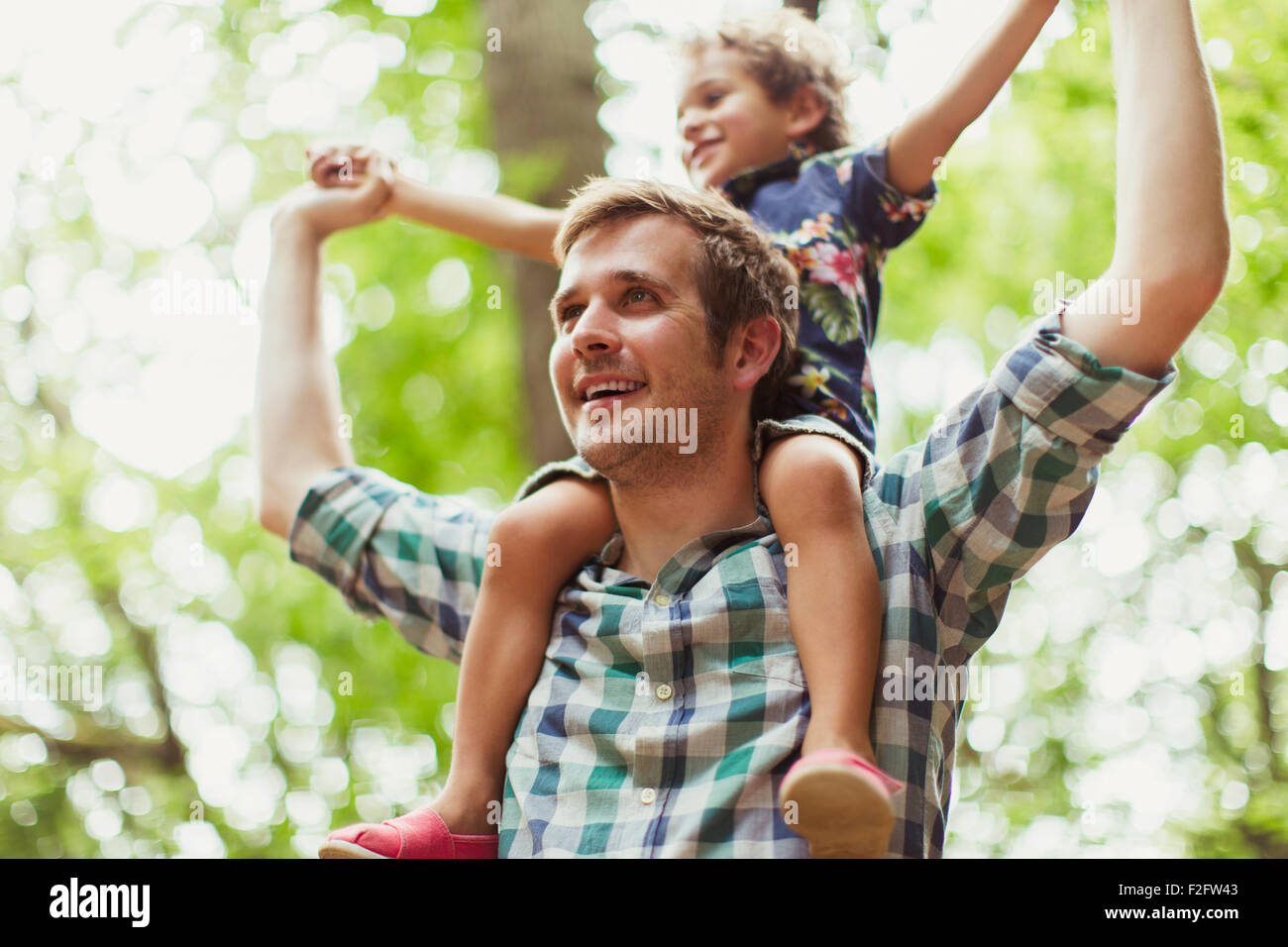 Father carrying son on shoulders below trees Stock Photo