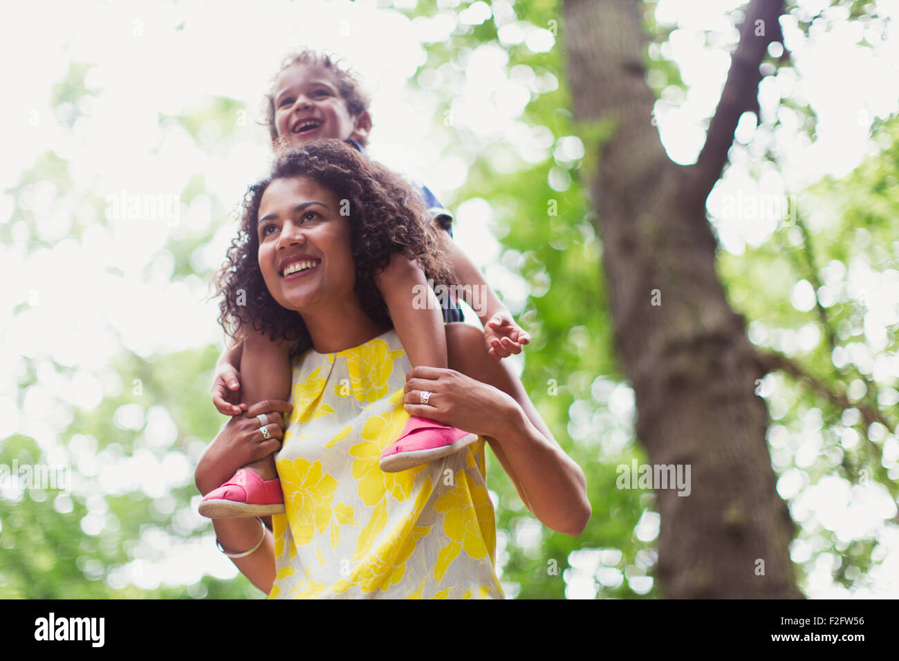 Smiling mother carrying son on shoulders below tree Stock Photo