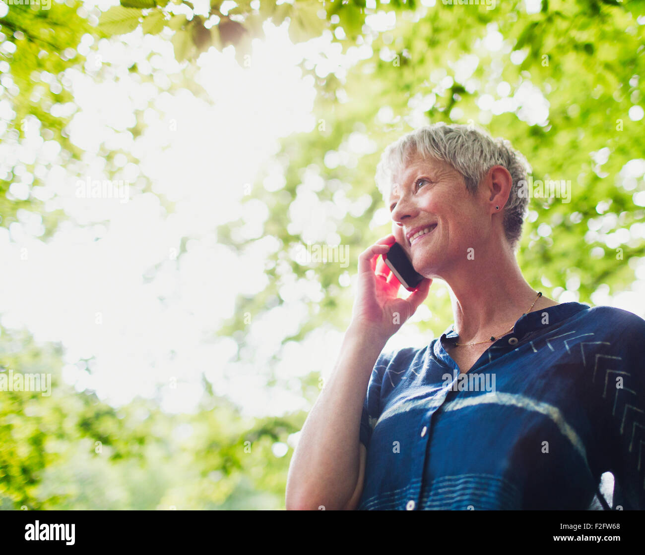 Smiling senior woman talking on cell phone below trees Stock Photo - Alamy