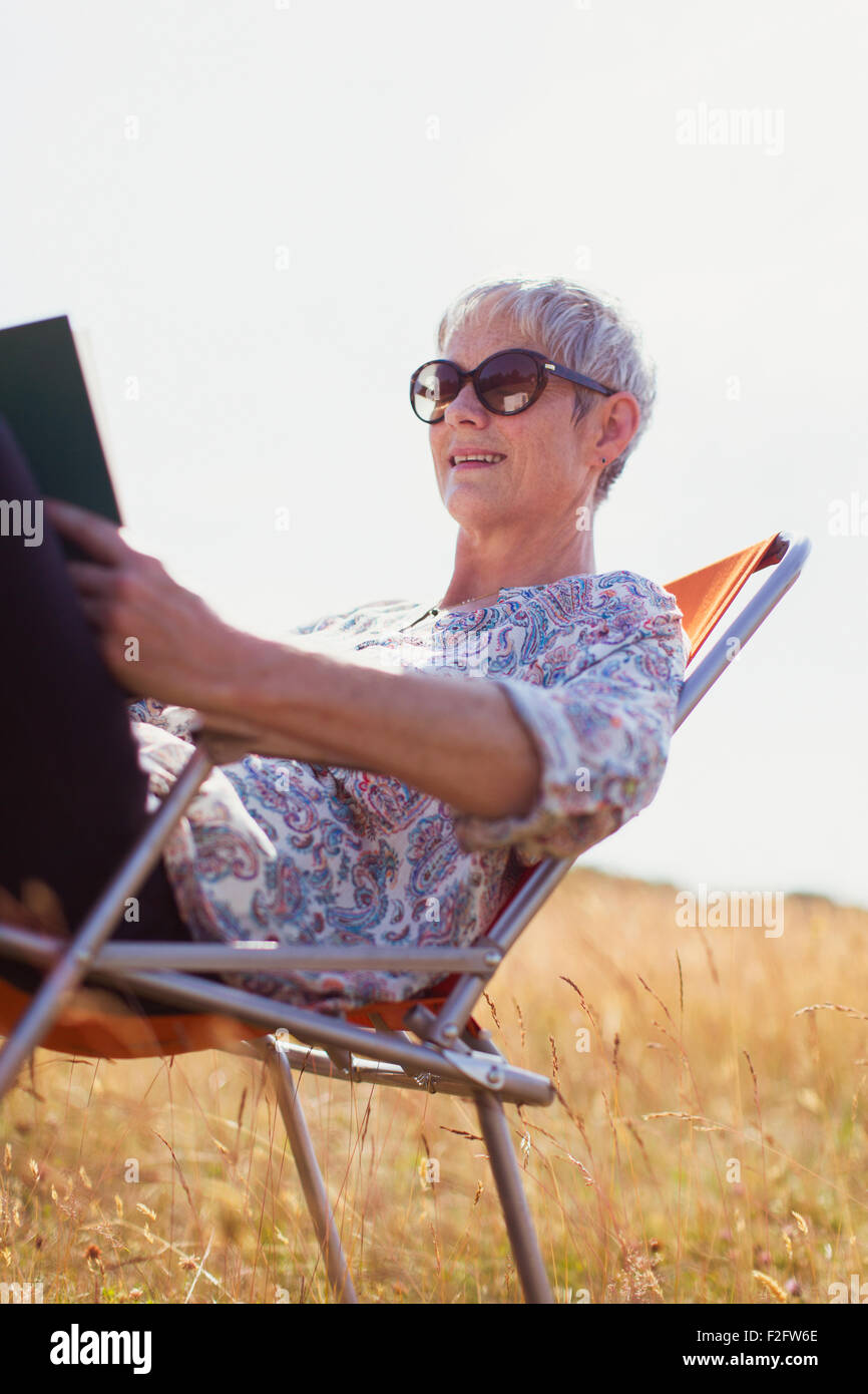 Senior woman reading book in sunny field Stock Photo