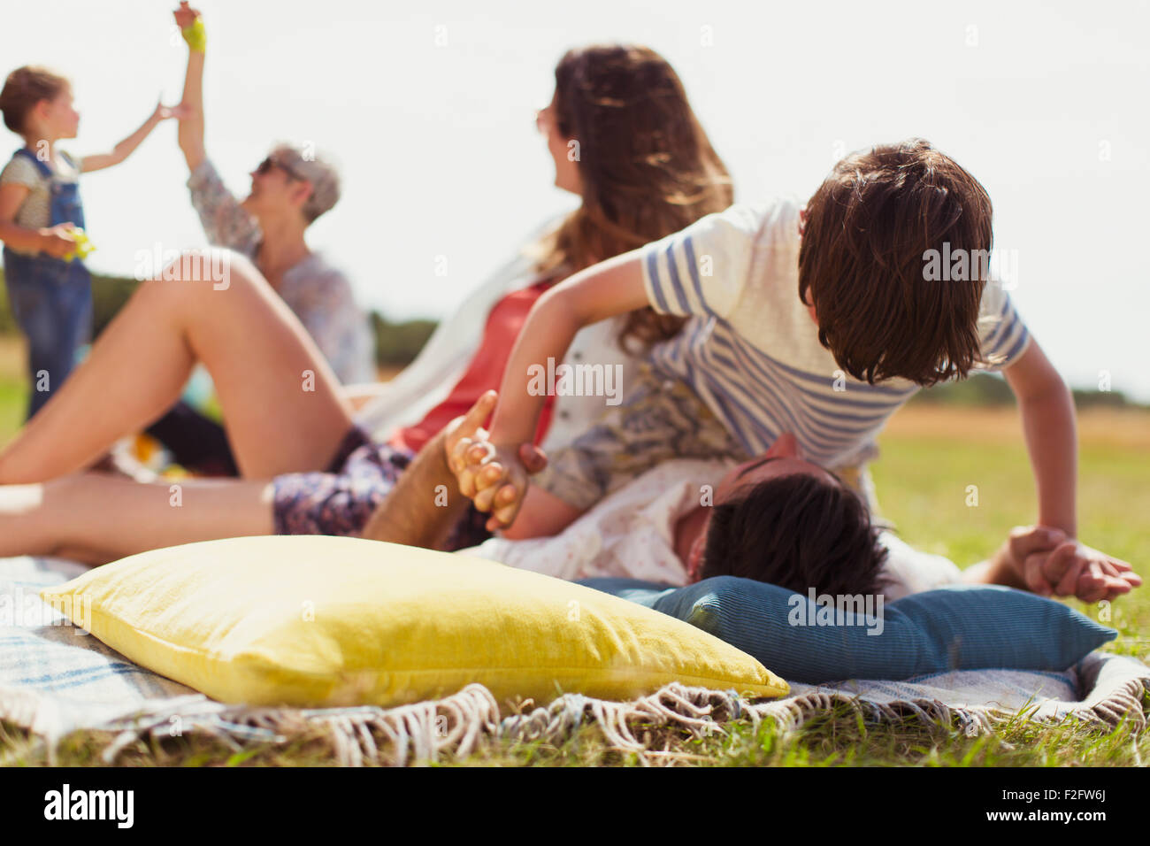 Playful son balancing on top of father in sunny field Stock Photo