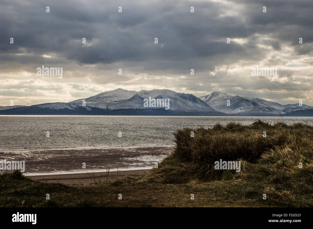 Snow covered mountain, Goatfell, on Arran with grass and beach in foreground. Stock Photo