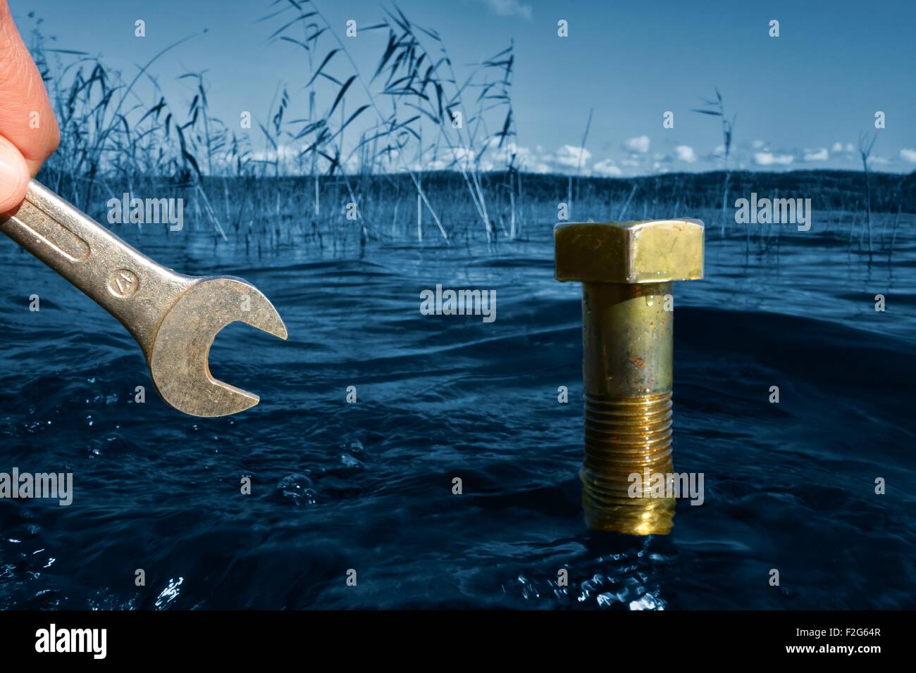 Environmental concept: Hand with a wrench in front of a large bolt in a lake. Stock Photo