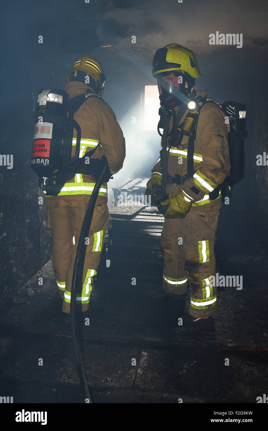 Firefighters in breathing apparatus extinguish a fire in a smoke filled building. Dark, smoke filled room moody lighting. Stock Photo