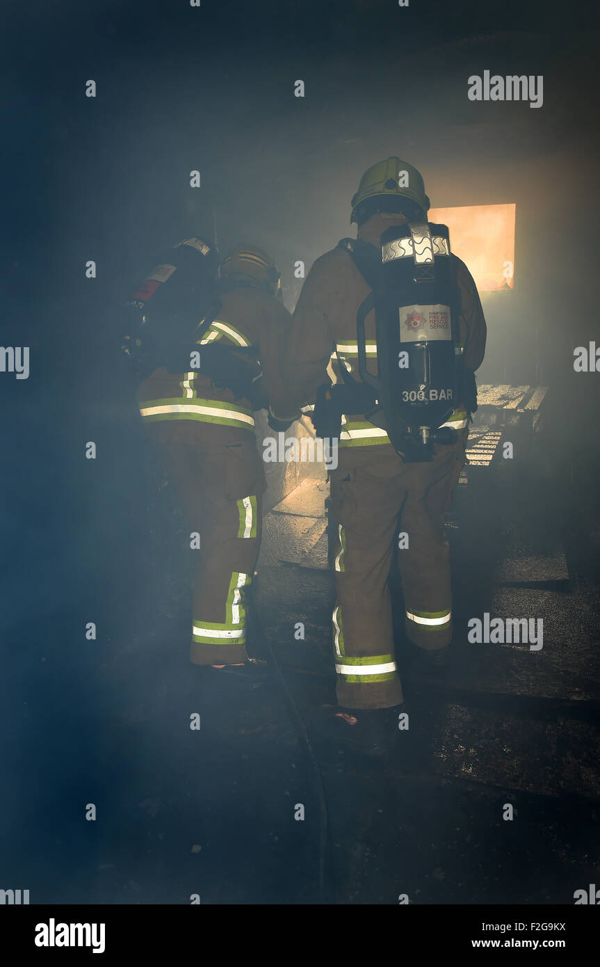 Firefighters in breathing apparatus extinguish a fire in a smoke filled building. Dark, smoke filled room moody lighting. Stock Photo