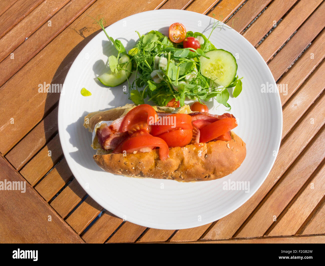 Lunchtime snack Brie cheese and bacon  sandwich in aseedy bread roll with mixed salad Stock Photo