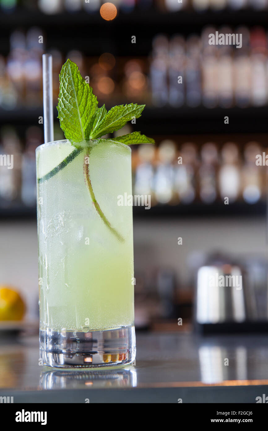 vertical of cocktail in tall glass with cucumber and mint garnish in bar Stock Photo