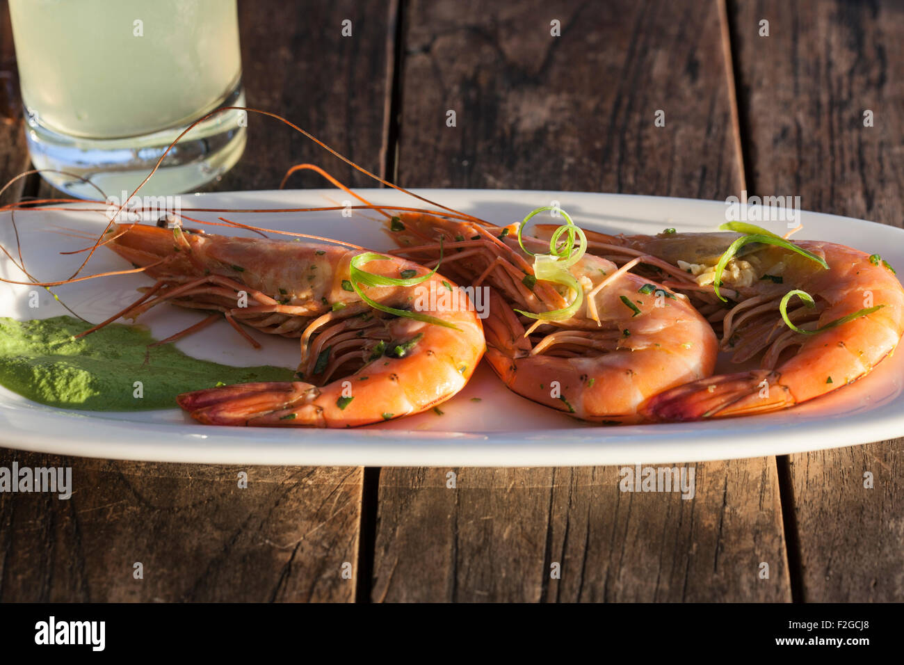 three large shrimp on white platter with drink, side lit with drink on rustic table Stock Photo