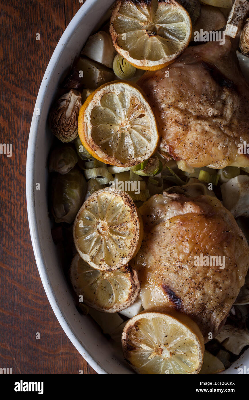 overhead view of roasted chicken thighs in oval baking dish with lemons and brussel sprouts Stock Photo