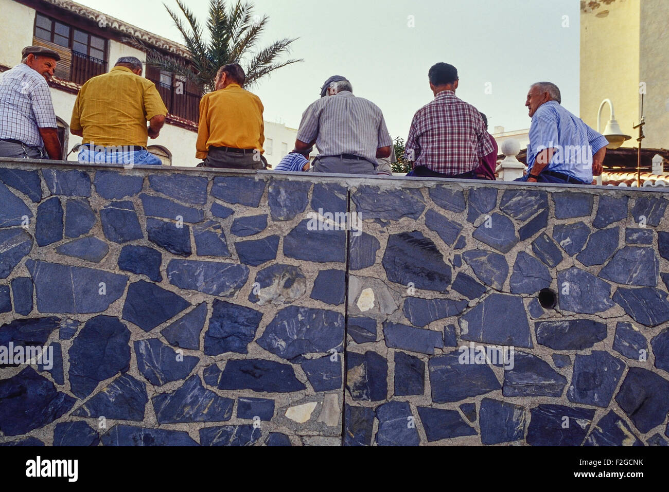 A group of local male villagers sitting on wall. Castell De Ferro. Spain. Europe Stock Photo