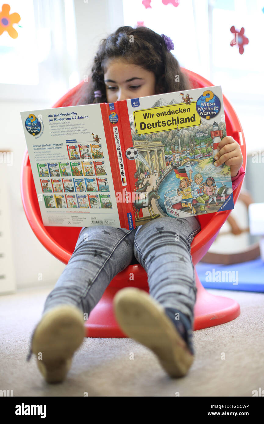 A refugee reads a donated book during a media event in Bremer Strasse kindergarten of a centralised initial processing station (ZEA) for refugees set up by the German Red Cross (DRK) in Hamburg, Germany 18 September 2015. Children from Bremer Strasse kindergarten are part of the 'Aktion Zusammenspiel - Buendnisse für junge Fluechtlinge' (lt: Play Together Campaign - Alliances for Refugee children). The focus of the Germany-wide campaign is interaction between refugee children and German children. Photo: Christian Charisius/dpa Stock Photo