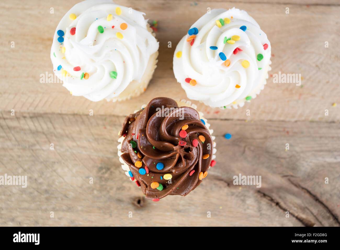 Homemade white and chocolate cupcakes against weathered wood background. Stock Photo