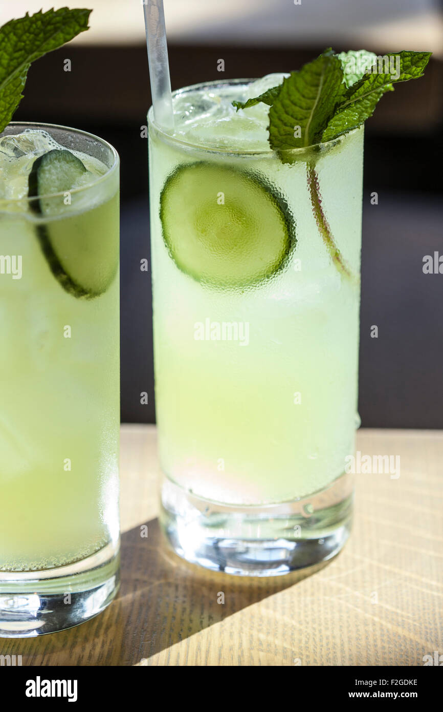 two cocktails in the sun in tall glasses garnished with mint and cucumber Stock Photo