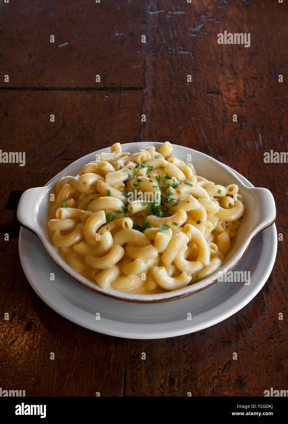 vertical shot of macaroni and cheese in shallow bowl and saucer with chopped parsley on wood table Stock Photo