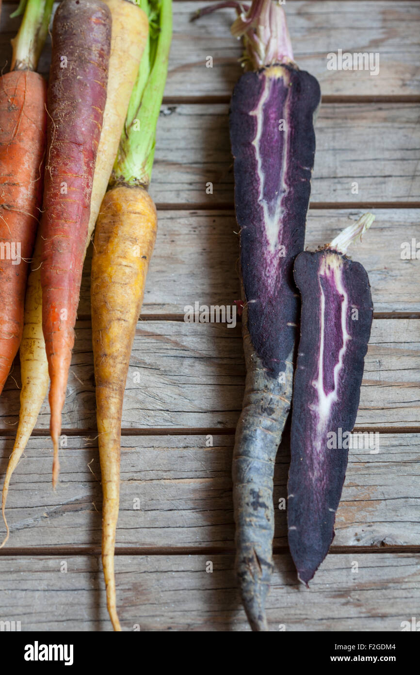 a bunch of rainbow carrots on rustic wood background, the purple carrot sliced vertically Stock Photo