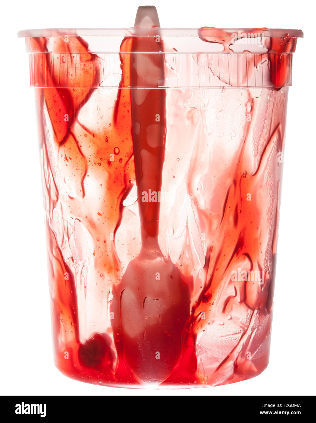 a translucent almost empty plastic container of red jam with a plastic spoon in the center Stock Photo