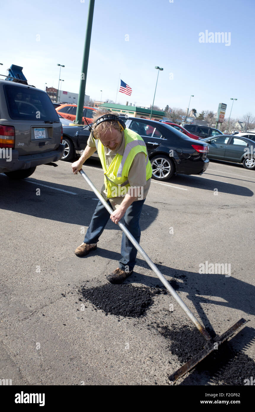 Maintenance man smoothing asphalt on patched potholes in city parking lot. St Paul Minnesota MN USA Stock Photo