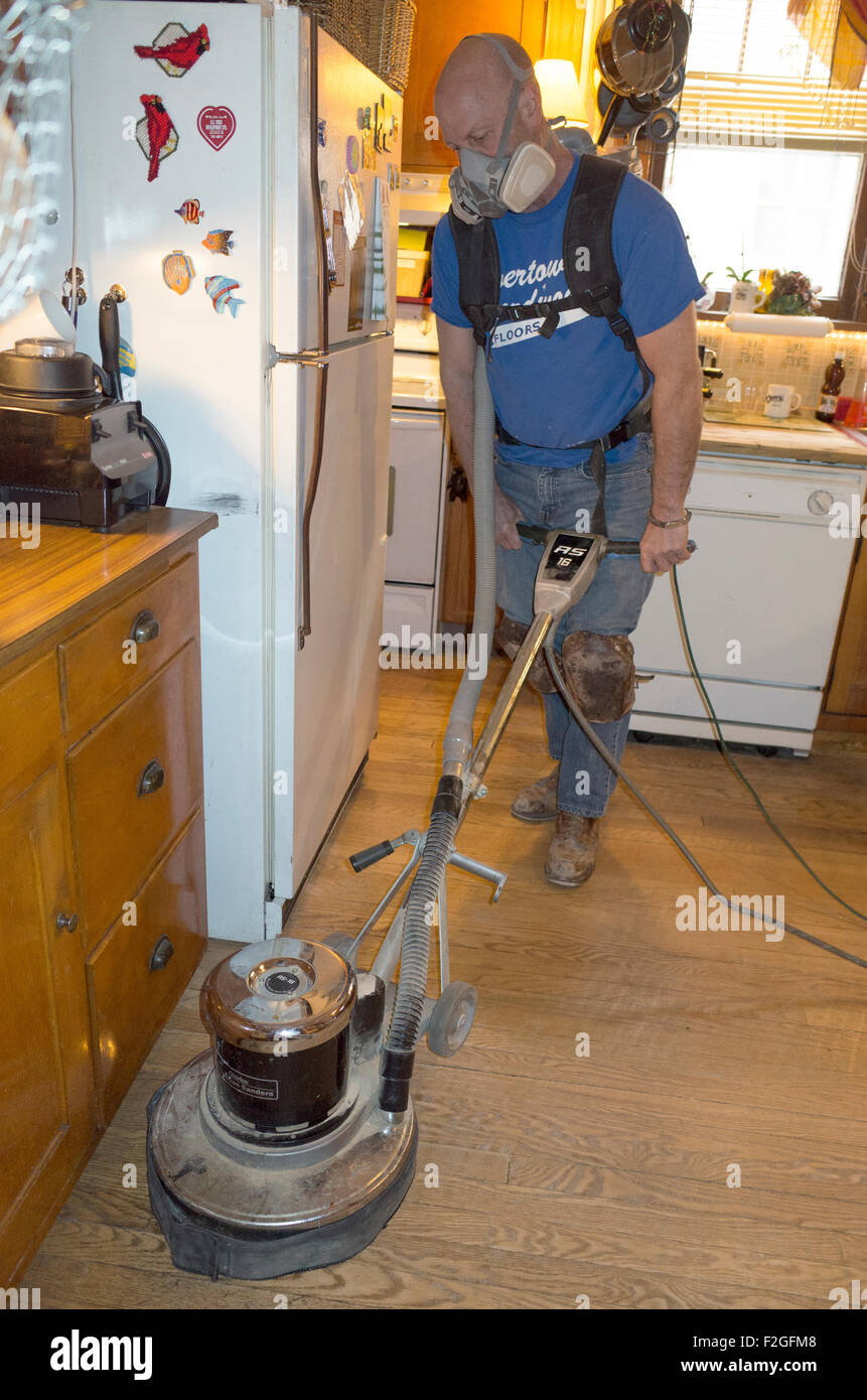 Man sanding oak hardwood floors wearing protective breathing filter mask and knee pads. St Paul Minnesota MN USA Stock Photo