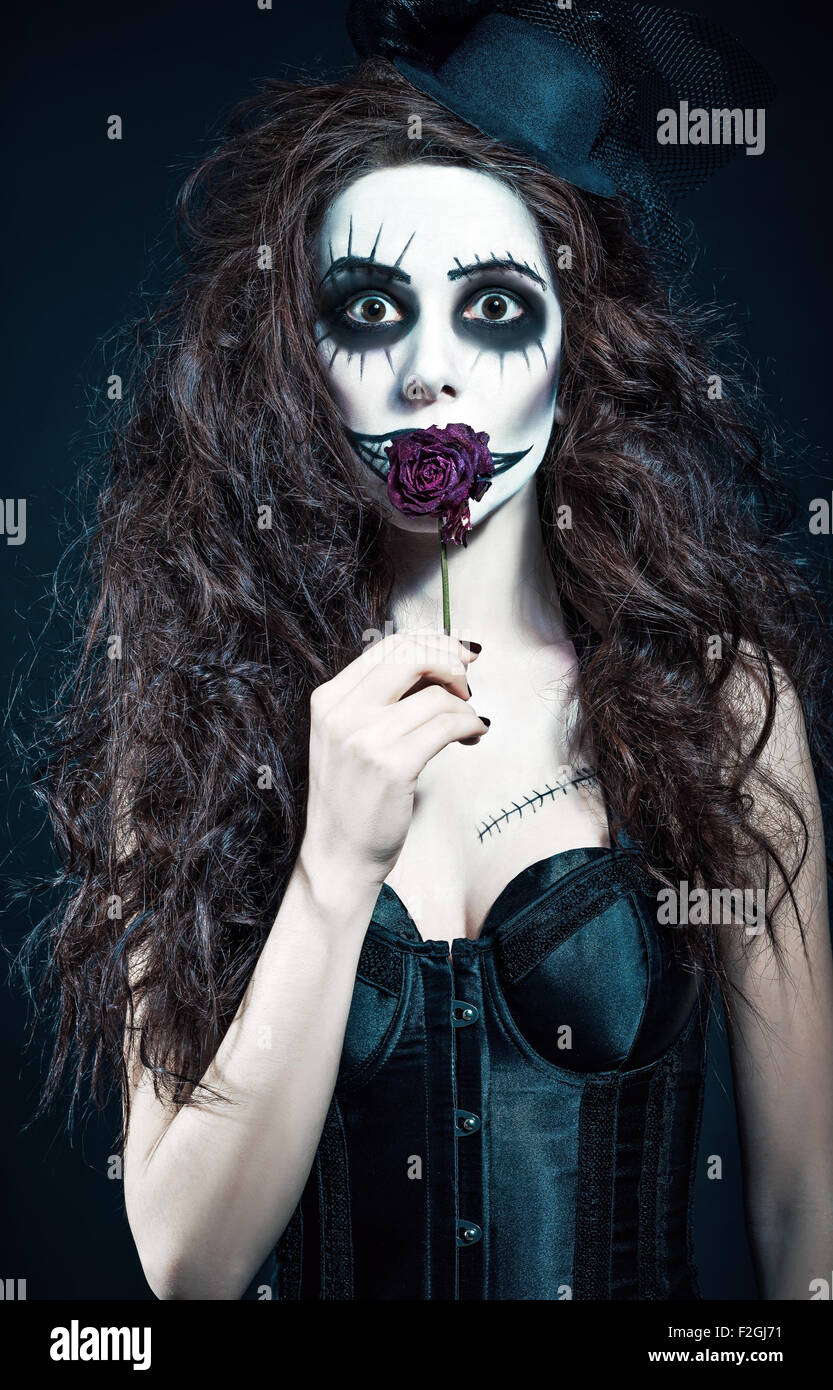 Young woman in the image of a sad gothic freak clown holds withered flower Stock Photo