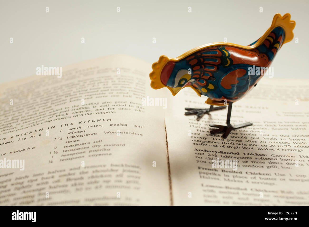 An antique metal toy chicken poses on an old cookbook. Stock Photo