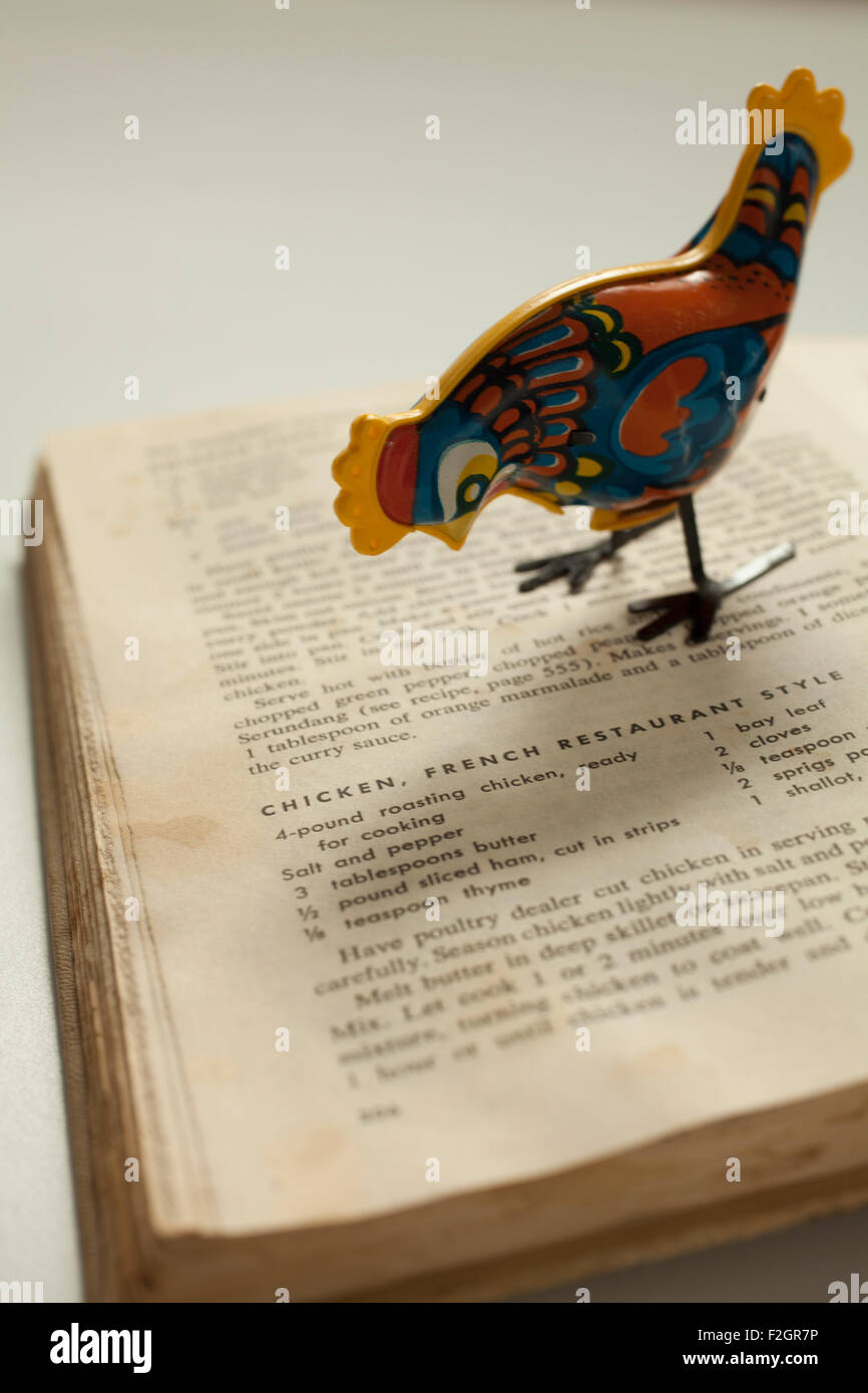 An antique metal toy chicken poses on an old cookbook. Stock Photo