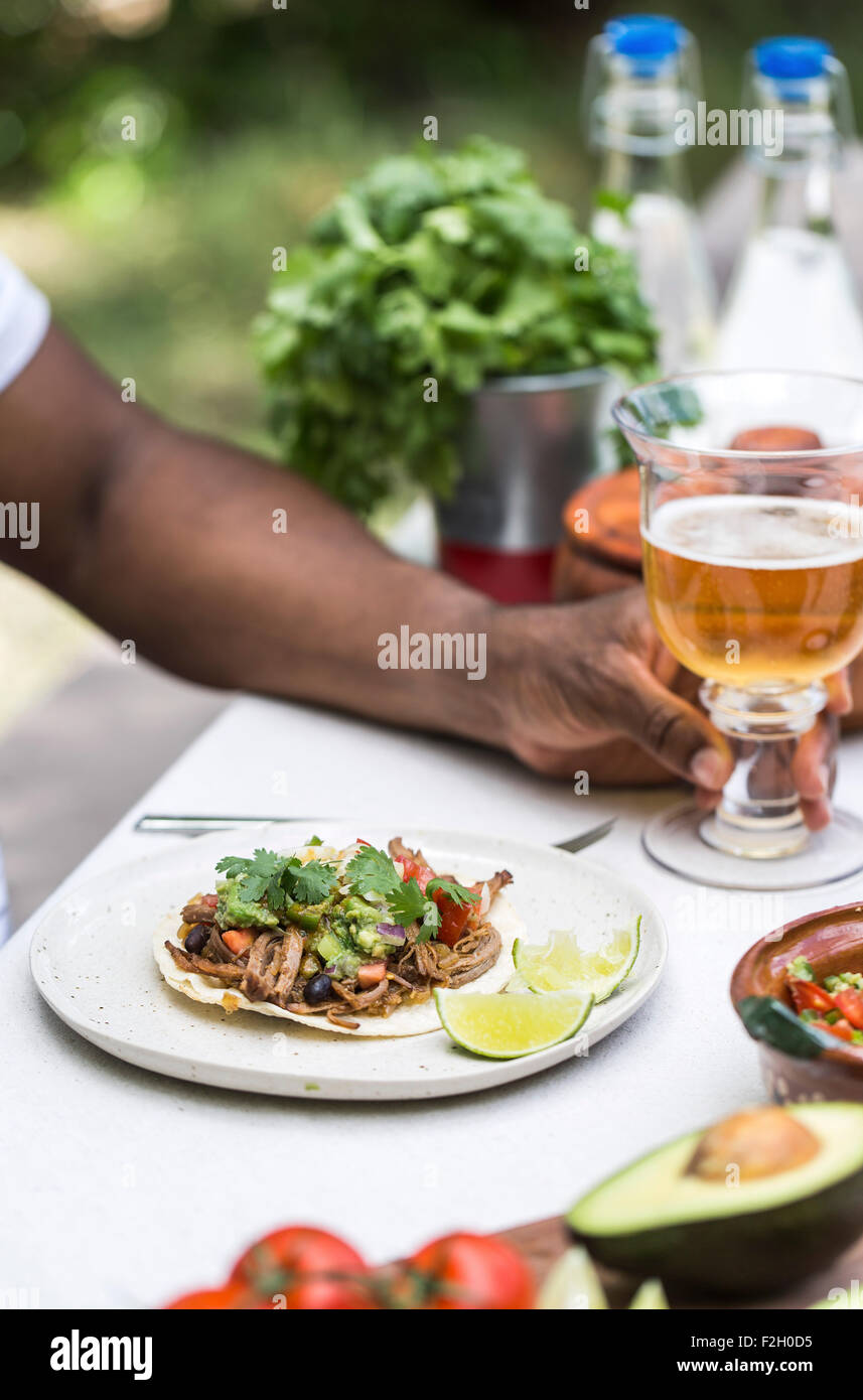 A slow cooked beef brisket chili taco served to a person in a picnic table with beer. Stock Photo