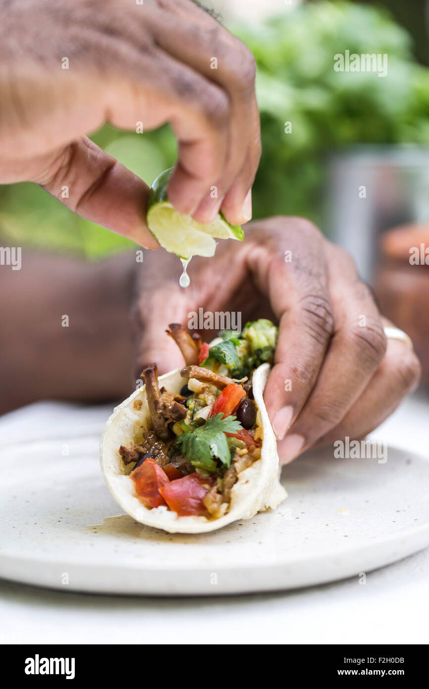 A man is squeezing lime on a slow cooked beef brisket chili taco while holding it with his other hand. Stock Photo