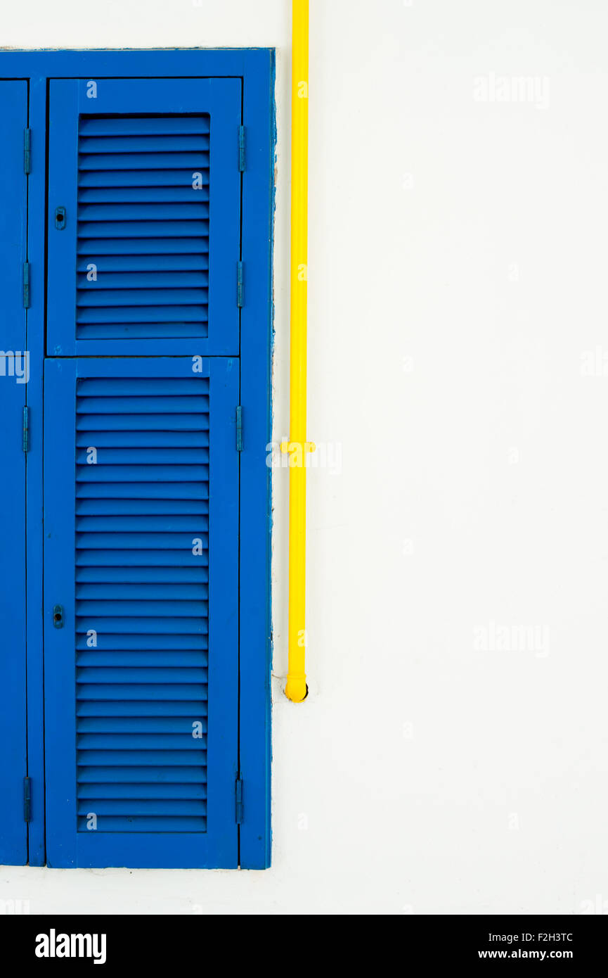 Part of blue shutter window and yellow tube on white wall with copyspace Stock Photo