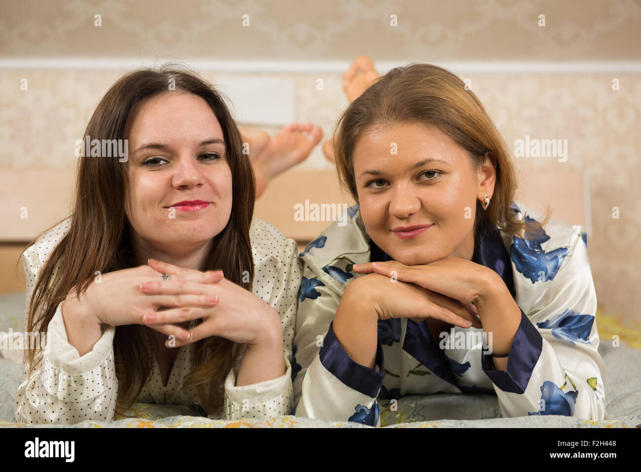 Two girlfriends laying in pajamas in bed and looking at camera Stock Photo