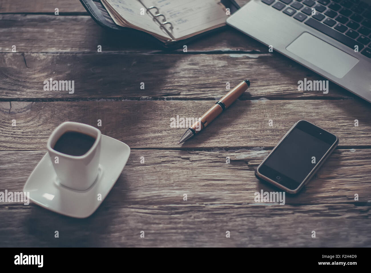 vintage composition of modern wooden table desk with smartphone laptop and cup of coffee with focus on pen and small DOF Stock Photo