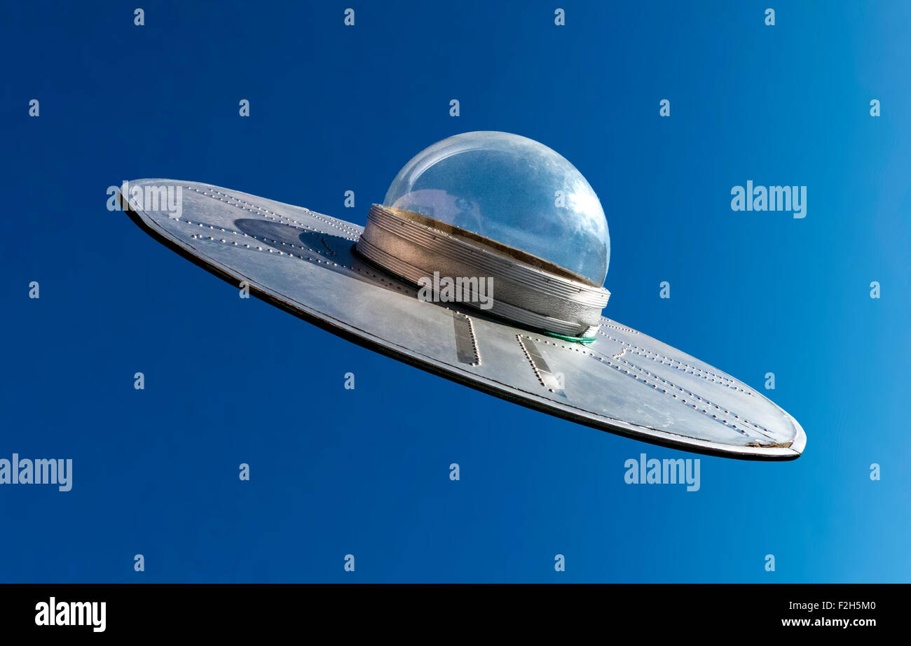 A knockout image of a flying saucer with a domed cockpit on a blue sky background. Stock Photo