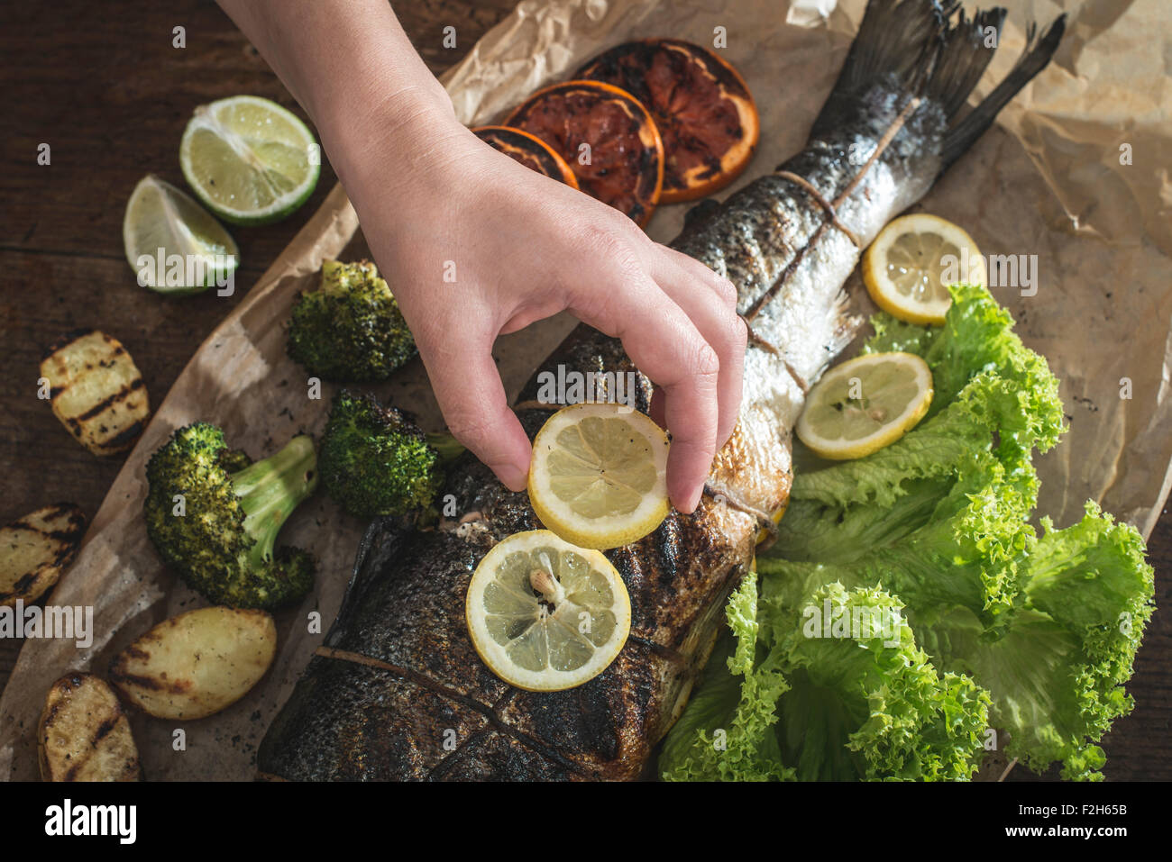 Roasted salmon and vegetables. Hand putting lemon on fish Stock Photo