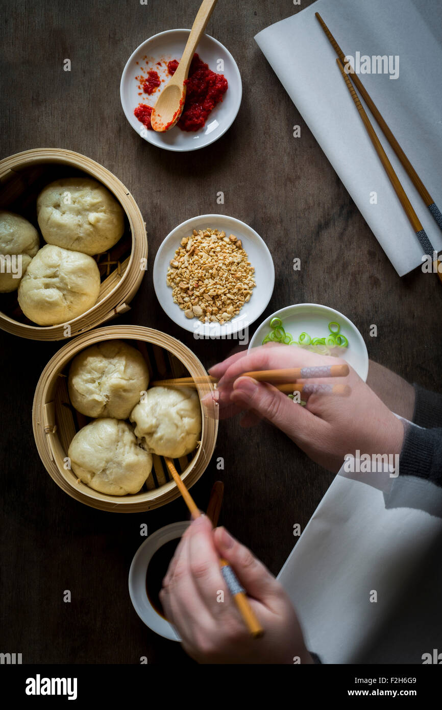 Woman's hands serving steamed dumplings from bamboo steamers on wooden