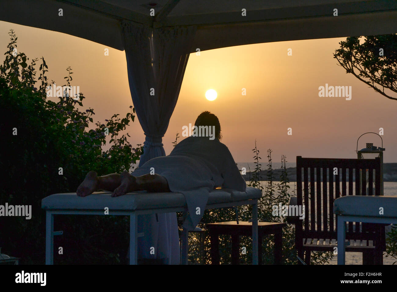 Woman lying down on massage table in outdoor spa at Cyprus, at sunset