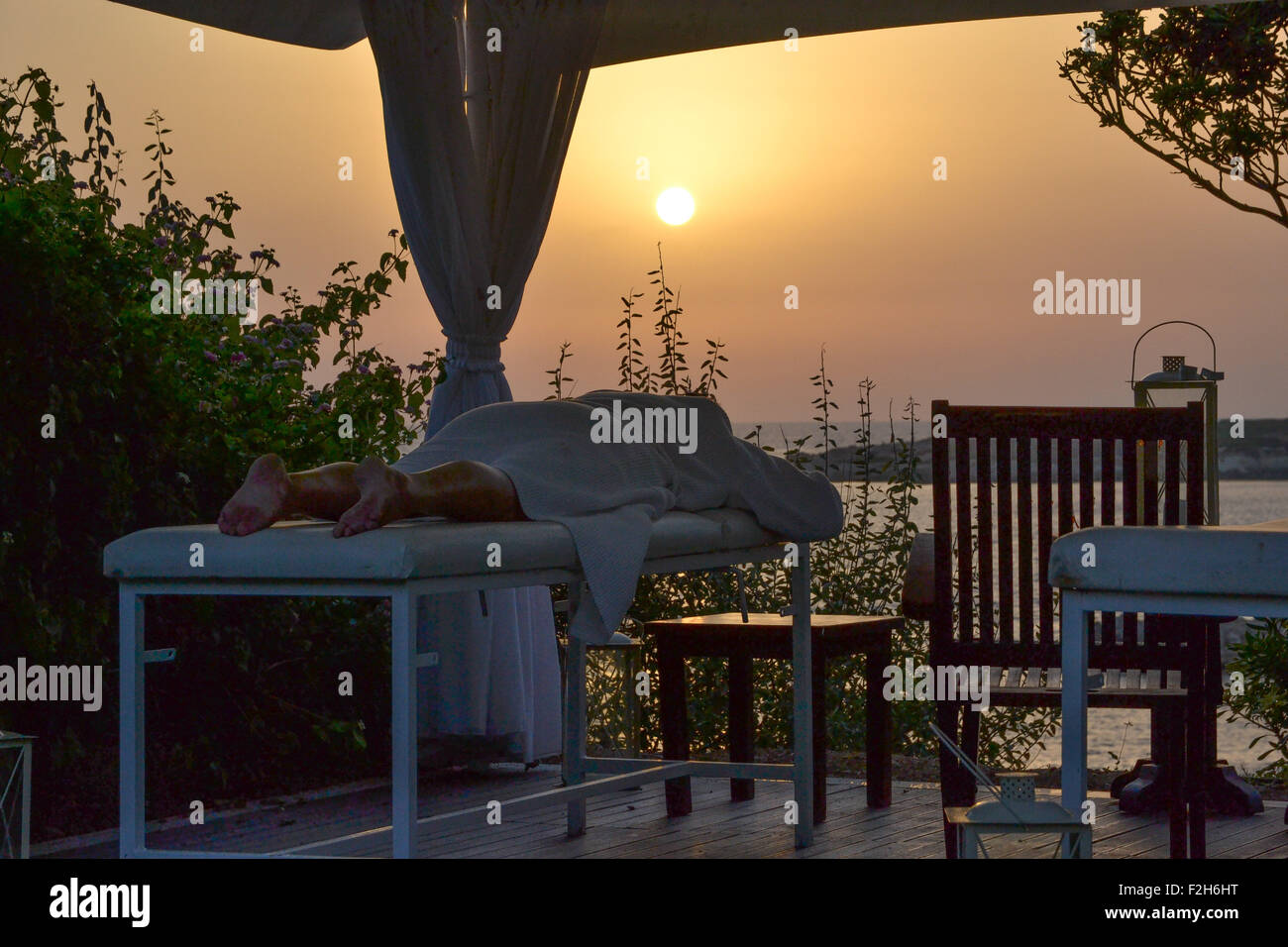 Woman lying down on massage table in outdoor spa at Cyprus, at sunset