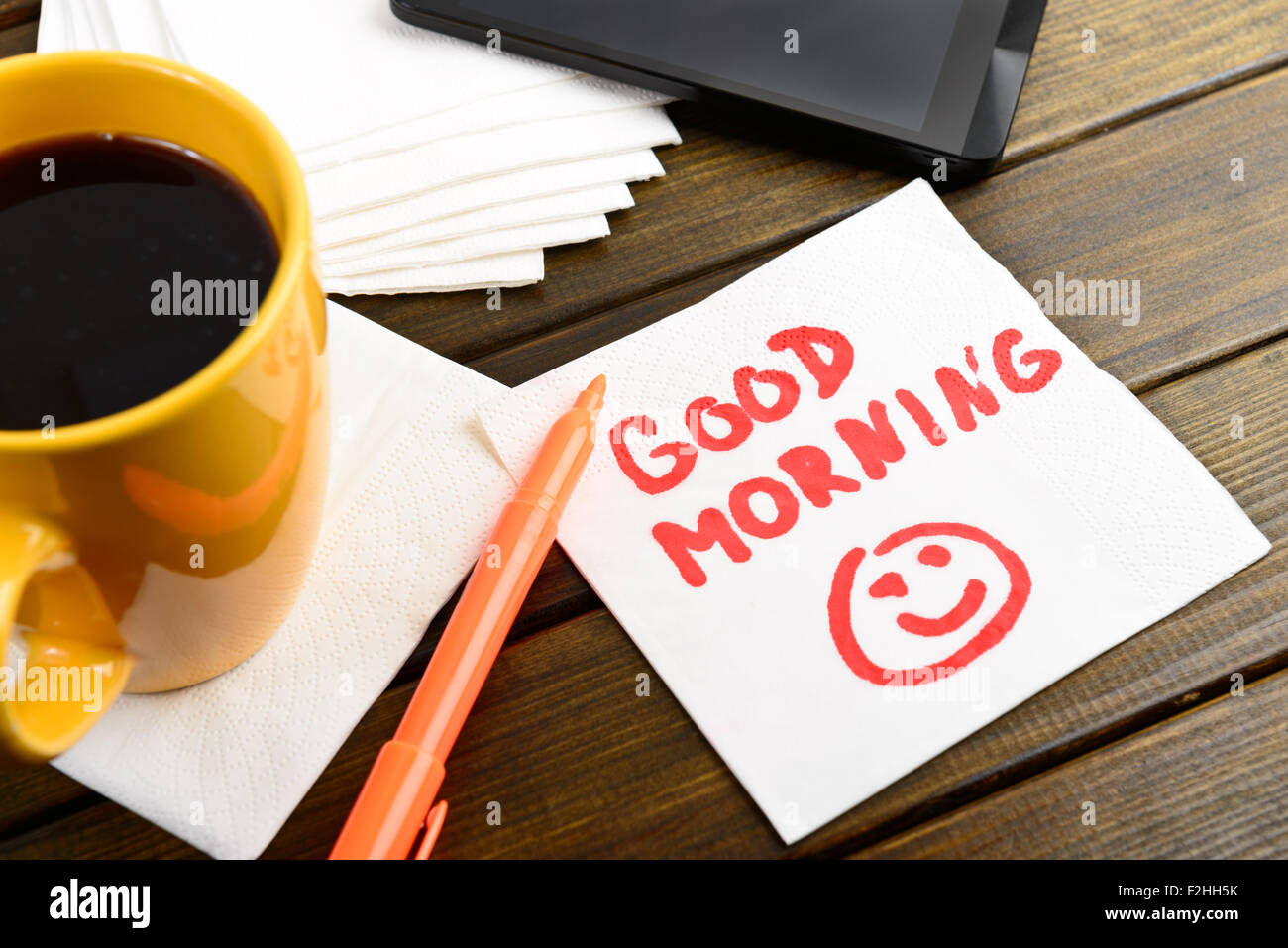 Good morning writing on white napkin around coffee pen and phone on wooden table Stock Photo