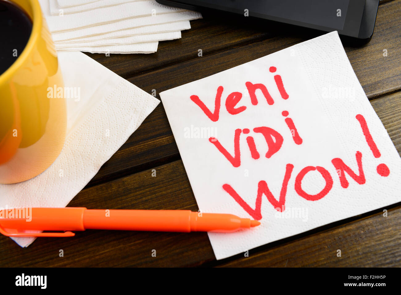 Veni vidi won writing on white napkin around coffee pen and phone on wooden table Stock Photo
