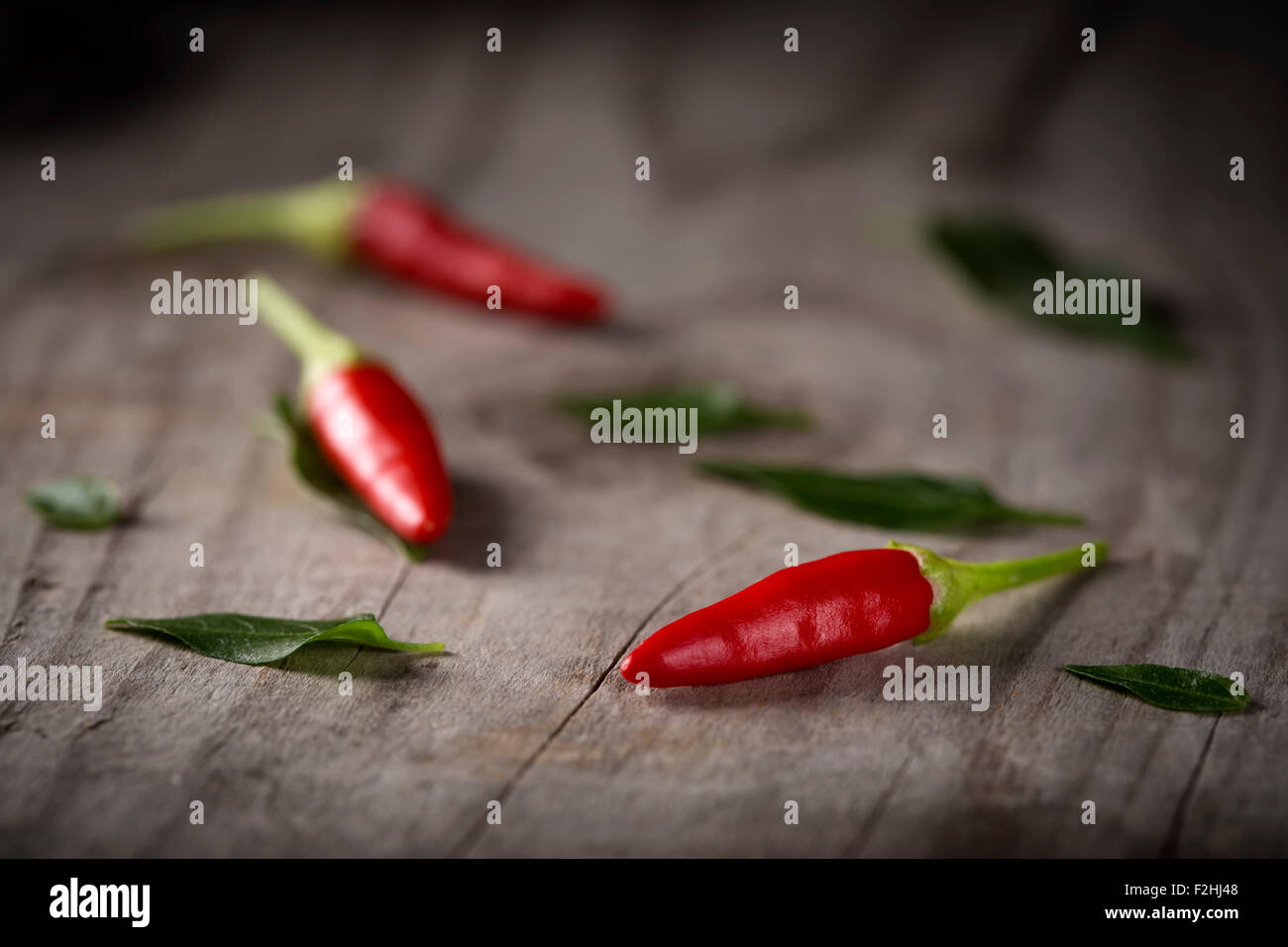 Red hot chili peppers on wood background with leaves Stock Photo