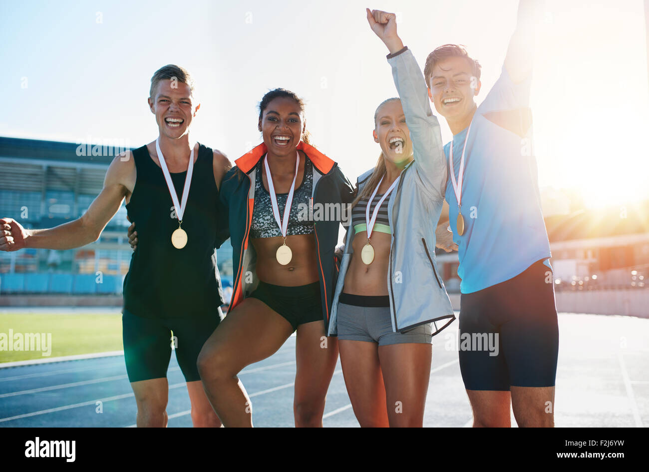 Portrait of ecstatic young athletes together with medals. Group of runners standing together smiling with their hands raised in Stock Photo