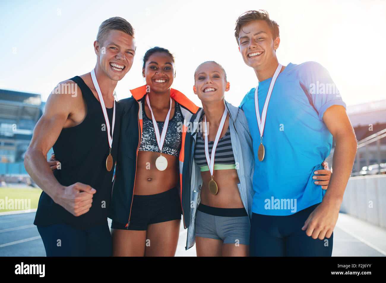 Happy multiracial athletes celebrating victory while standing together on racetrack. Group of runner with medals winning a compe Stock Photo