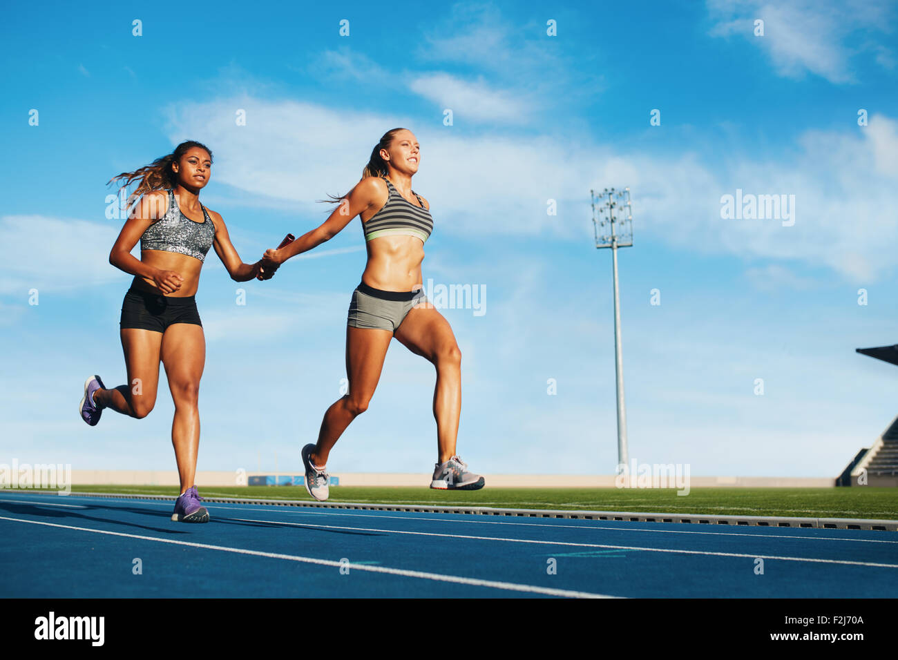 Young woman running a relay race and giving relay baton to her teammate