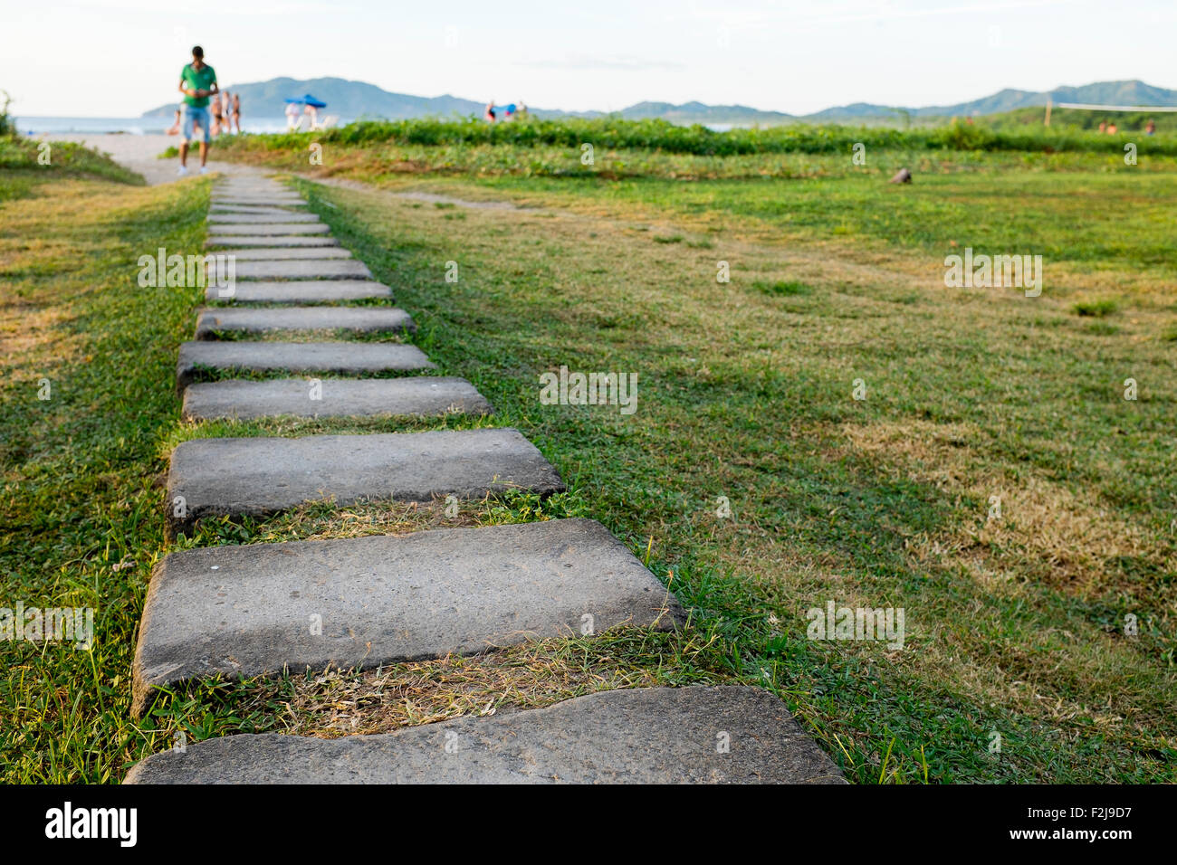 A path lined with paving stones leads out from Witches Rock Surf camp to Tamarindo beach across beach grass in Costa Rica Stock Photo