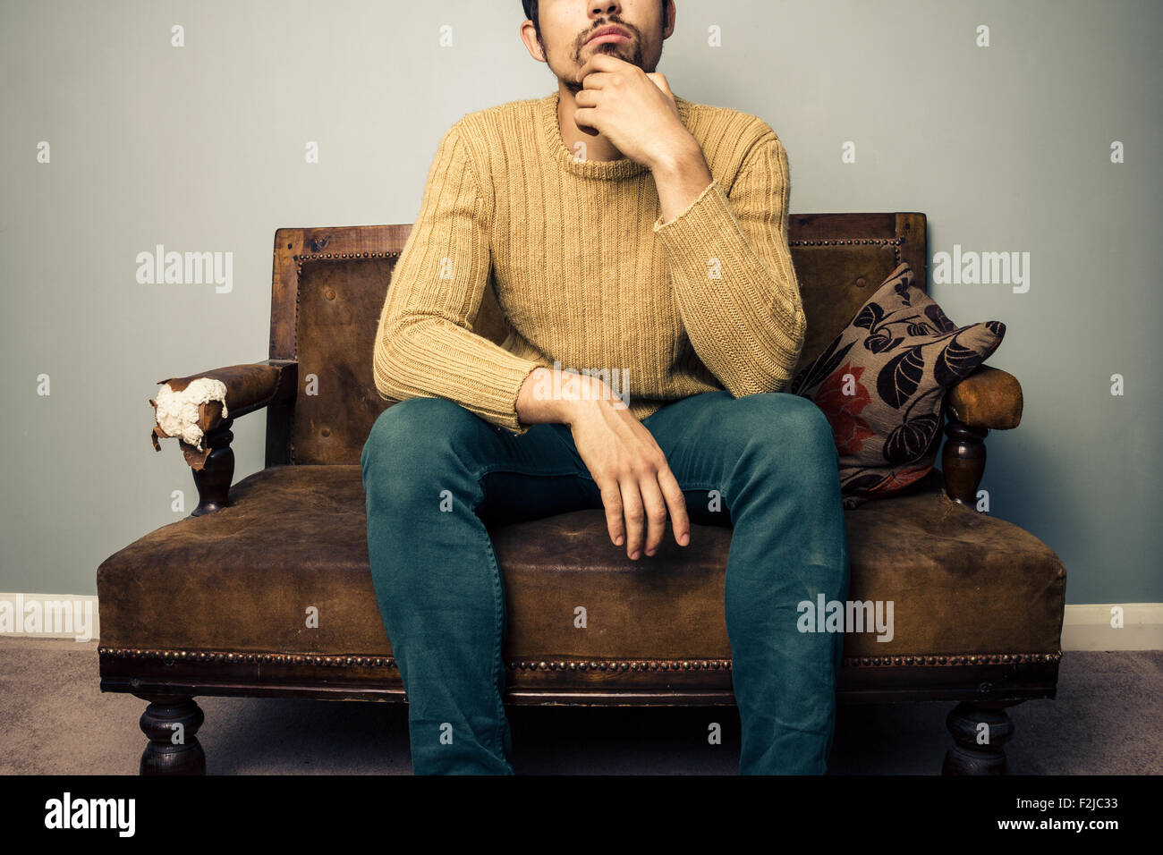 Young man sitting on sofa and thinking Stock Photo - Alamy